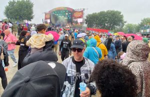 Cilvēku pūlis pie Summerjam festivāla skatuves lietainā dienā ar krāsainiem lietussargiem un lietusmēteļiem