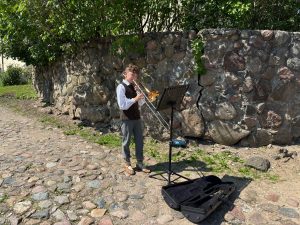 Zēns tautastērpā spēlē trombonu pie akmens sienas