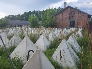 Betona piramīdas aizaugušā laukumā pie vecas ķieģeļu ēkas