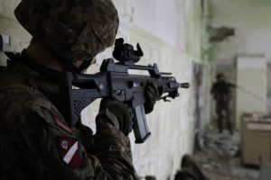 Zemessargs ar šauteni telpās, mērķējot uz izplūdušu figūru