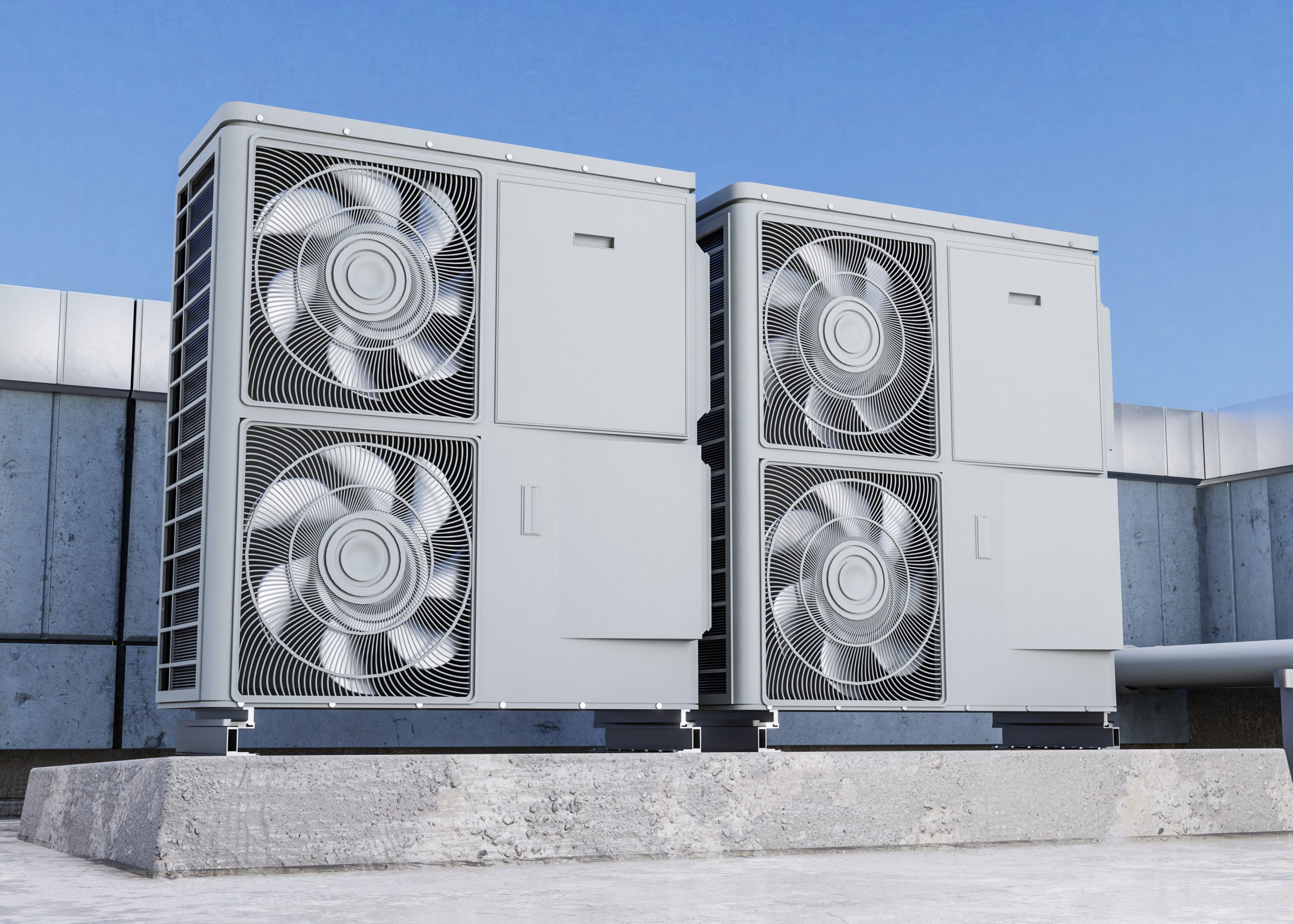 Divas pelēkas āra gaisa-ūdens siltumsūkņu vienības ar ventilatoriem, kas uzstādītas uz ēkas jumta vai pamatnes zem skaidrām debesīm.