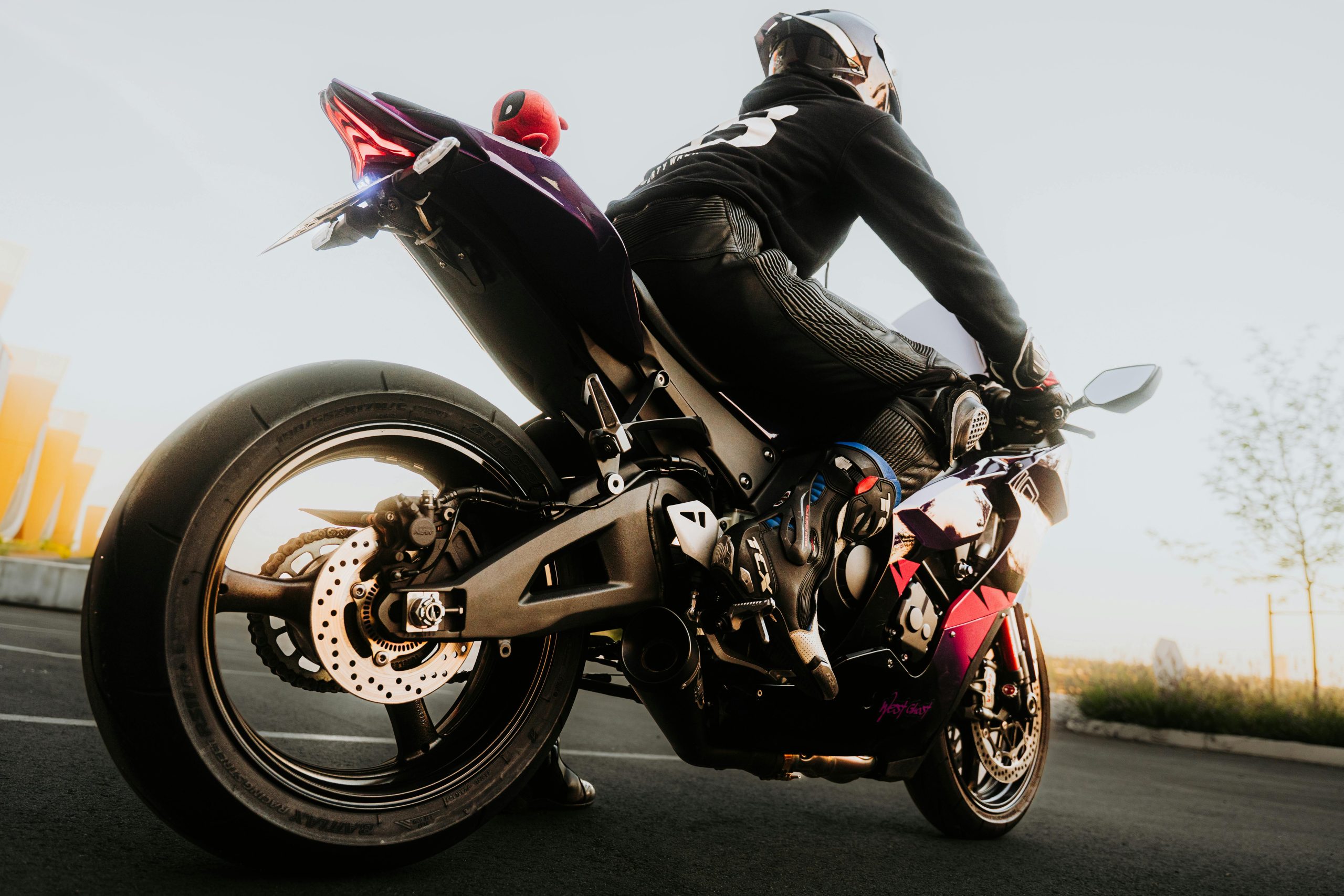 Motociklists pilnā ekipējumā sēž uz sporta motocikla, gatavs braucienam, ar zemu saules staru apgaismojumu.