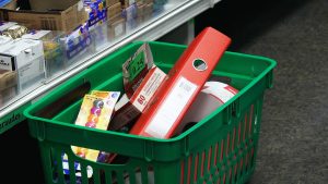 Zaļa iepirkumu groza saturs ar kancelejas precēm