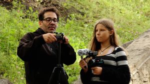 Vīrietis un meitene ar videokameru un statīvu filmēšanas nodarbībā dabā