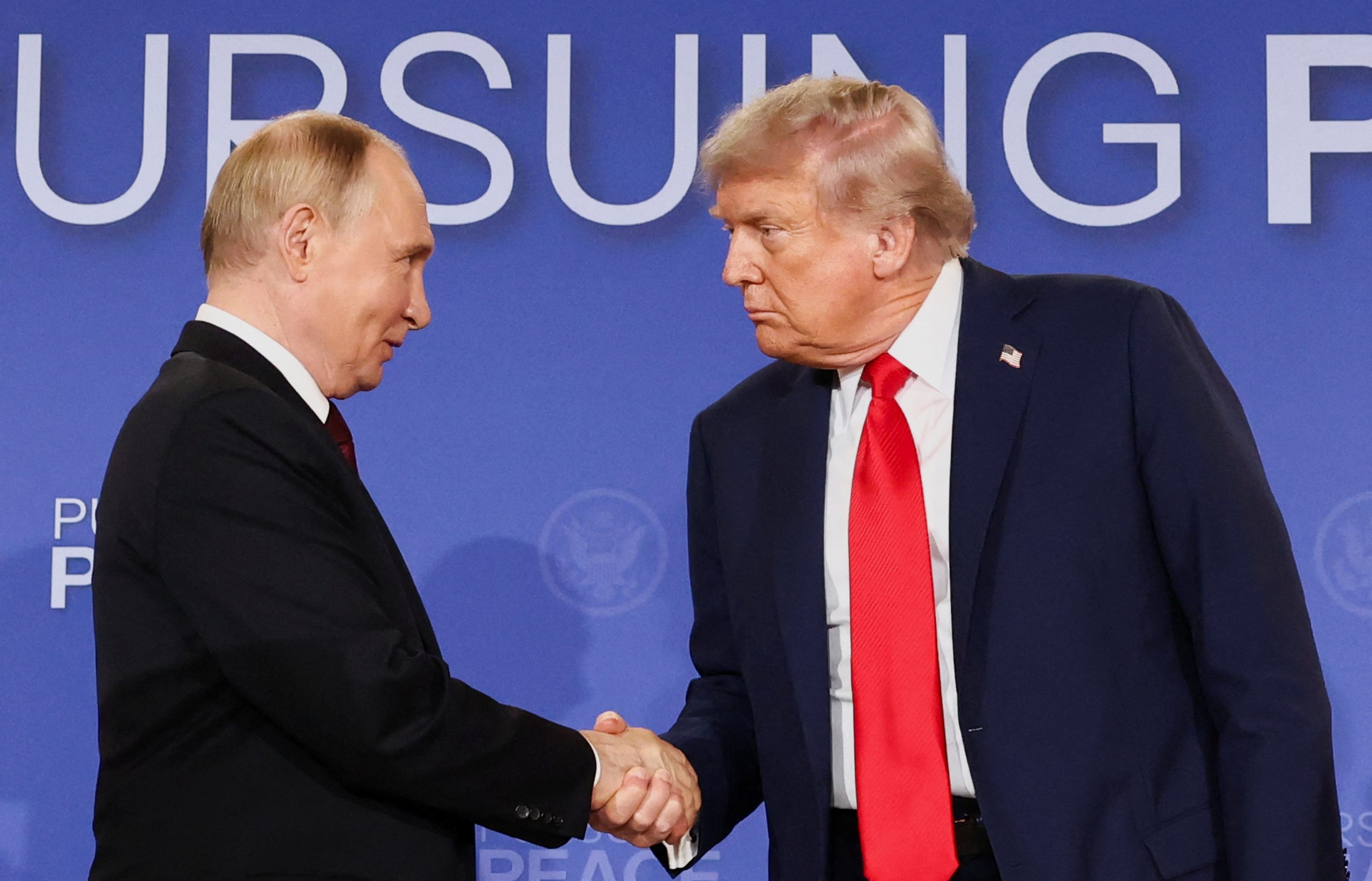 Vladimirs Putins un Donalds Tramps oficiālā pasākumā sarokojas uz zilas fona sienas