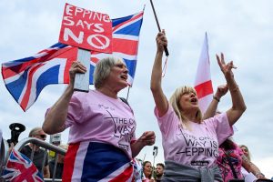 Sievietes vicina Lielbritānijas un Anglijas karogus protestā pret nelegālo imigrāciju. Viena sieviete tur plakātu ar uzrakstu "EPPING SAYS NO" (Epinga saka nē).