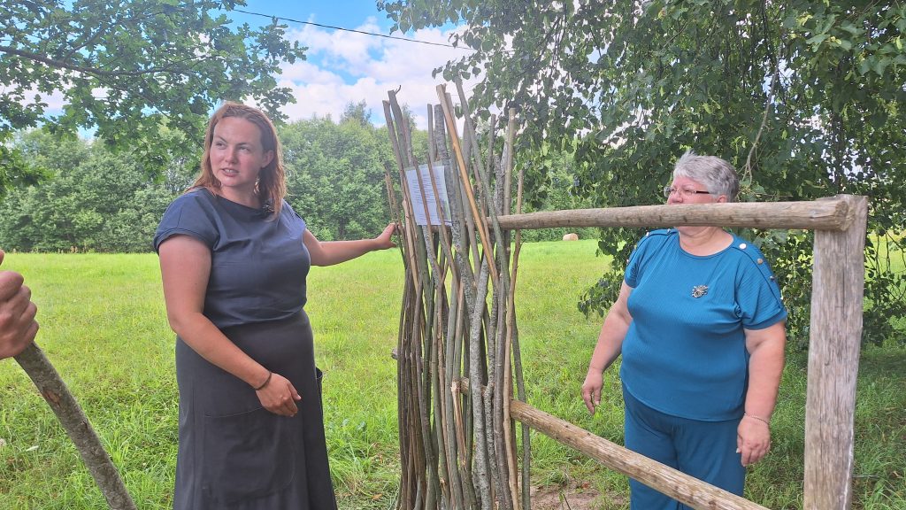 Sievietes stāv pie zedeņu žoga konstrukcijas un sarunājas