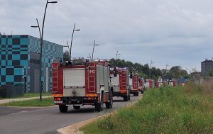 Ugunsdzēsēju autocilvēku kolonna pie rūpnieciskas ēkas