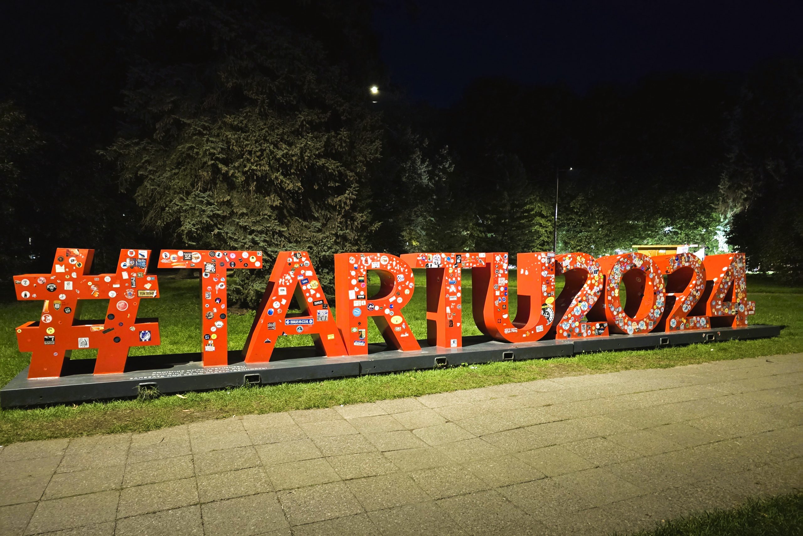 Liels sarkans uzraksts “#TARTU2024” naktī parkā.