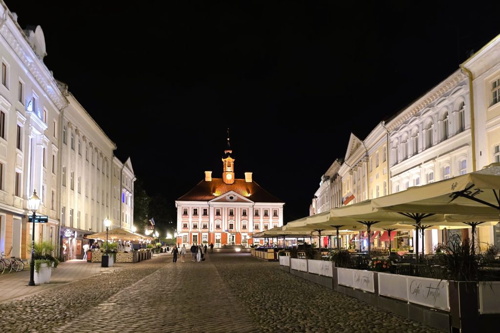 Tartu Rātslaukums naktī ar kafejnīcām un veikaliem.