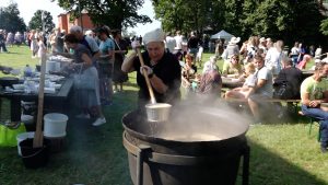 Sieviete brīvdabas festivālā pasniedz zupu no lielā katla