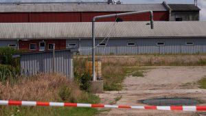 Slēgta rūpnieciska teritorija ar noliktavu ēkām un drošības lentu priekšplānā.