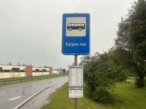 Autobusa pieturas zīme "Karjera iela" ar sarakstu lietainā dienā