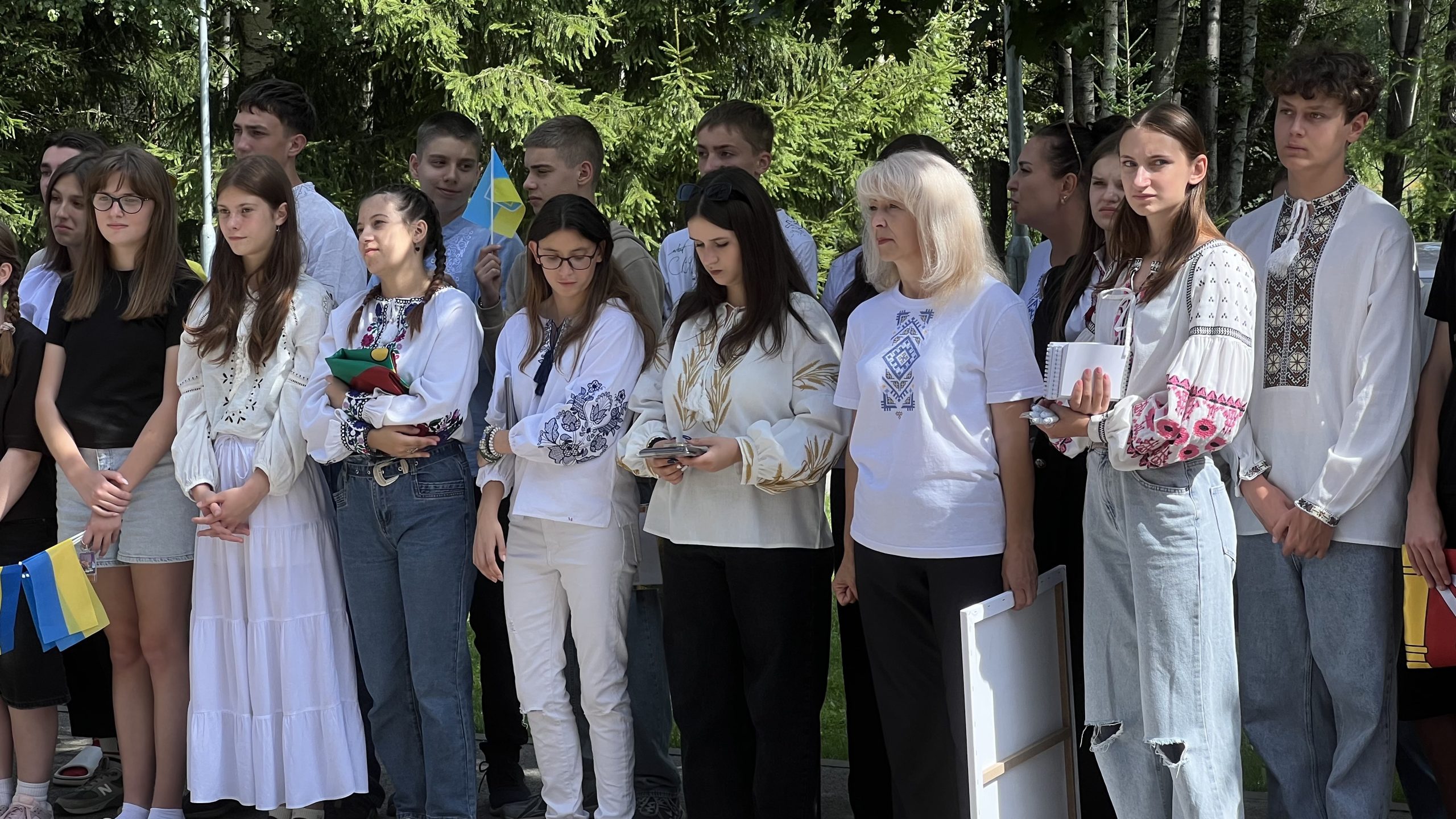 Cilvēku grupa tautiskos kreklos un ar Ukrainas karogiem