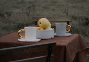Katrīnas Keramikas porcelāna krūzes ar zelta rokturiem un bļoda ar āboliem uz āra galda