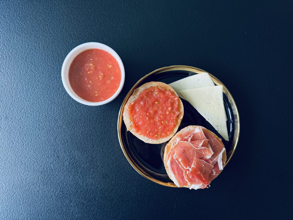 Gatavais pan con tomate ar jamón un rīvētu tomātu masu blakus.