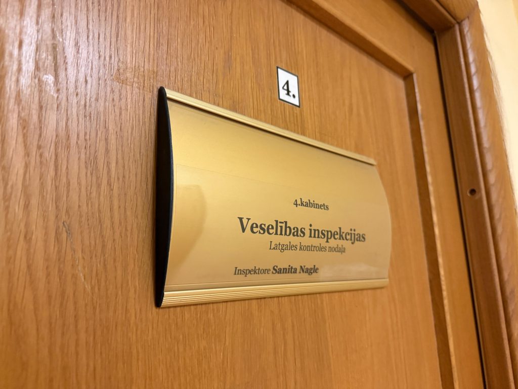 Koka durvis ar misiņa plāksni, uz kuras ir uzraksts "Veselības inspekcija" un "Latgales kontroles nodaļa", kā arī inspektora vārds un uzvārds Sanita Nagle.