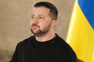 Ukrainas prezidents Volodimirs Zelenskis ar austiņu un Ukrainas karogu fonā