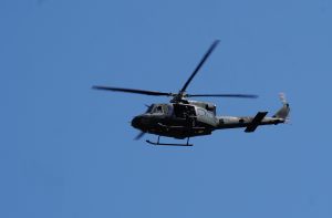 Militārais helikopters lido zilajās debesīs.