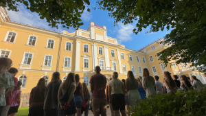 Jauniešu grupa pie vēsturiskās ēkas Latvijā vasaras skolas laikā.