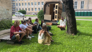 Vasaras skolas dalībnieki āra nodarbībā pie koka.