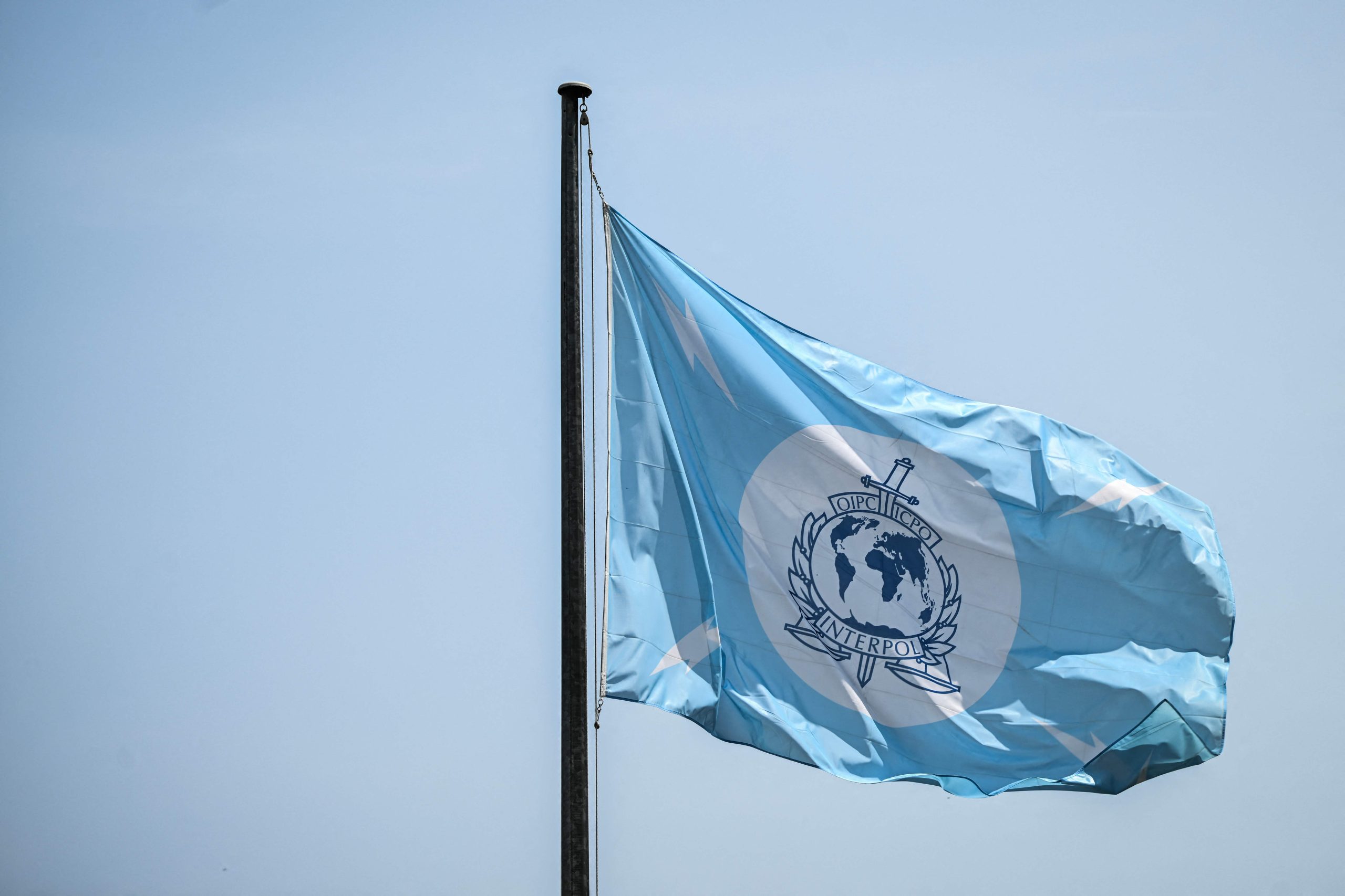 Interpol karogs plīvo vējā uz zila debesu fona.