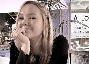 Anna Eihenbauma sēž pie galdiņa kafejnīcā, ar rokas balstu uz zoda