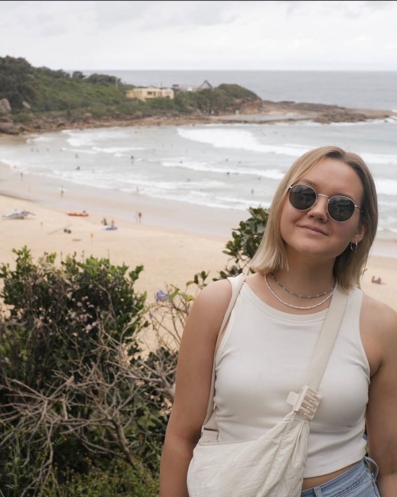 Anna Eihenbauma pozē pludmales fonā ar saulesbrillēm