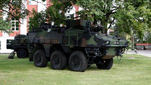 Militārā bruņumašīna stāv uz zāliena pie ēkas