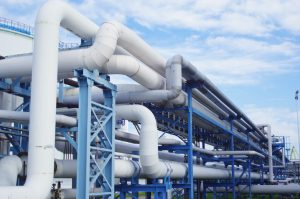 Naftas cauruļvads ar lielām industriālām caurulēm zilā metāla konstrukcijā saulainā dienā.