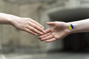 Divas rokas sniedzas viena otrai, uz rokas redzams Ukrainas karogs