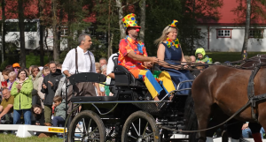 Klauni krāsainos tērpos zirgu pajūgā pasākuma laikā