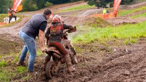 Motokrosa jaunais braucējs ar motociklu dubļainā trasē saņem palīdzību