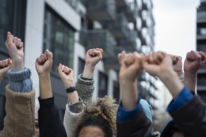Cilvēku paceltas dūres protestā starp mūsdienīgām ēkām.