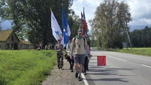 Svētceļnieku gājiens pa ceļmalu ar karogiem un krustu