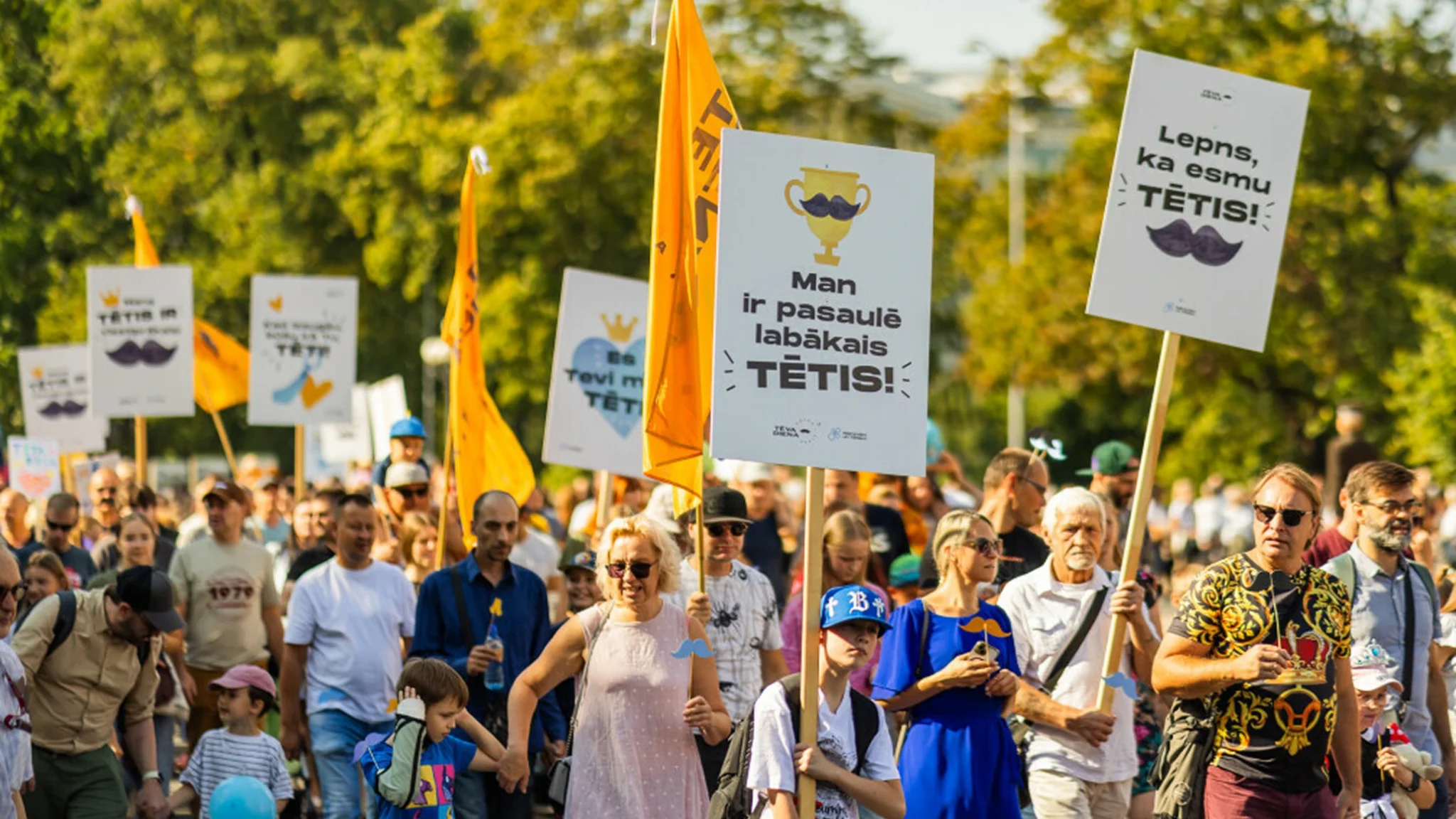 Cilvēki gājienā ar plakātiem, kas veltīti Tēva dienai.