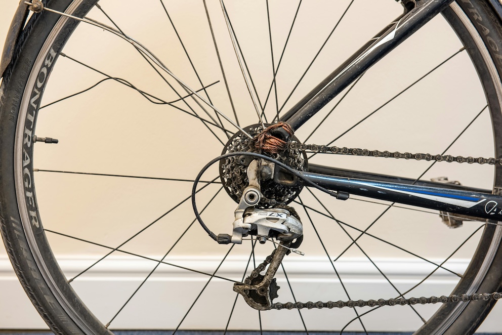Velosipēda aizmugurējais ritenis ar bojātu pārslēdzēju un apkopi nepieciešamām detaļām