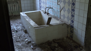 Pamesta vannas istaba ar vecu flīžu vannu un gružiem uz grīdas