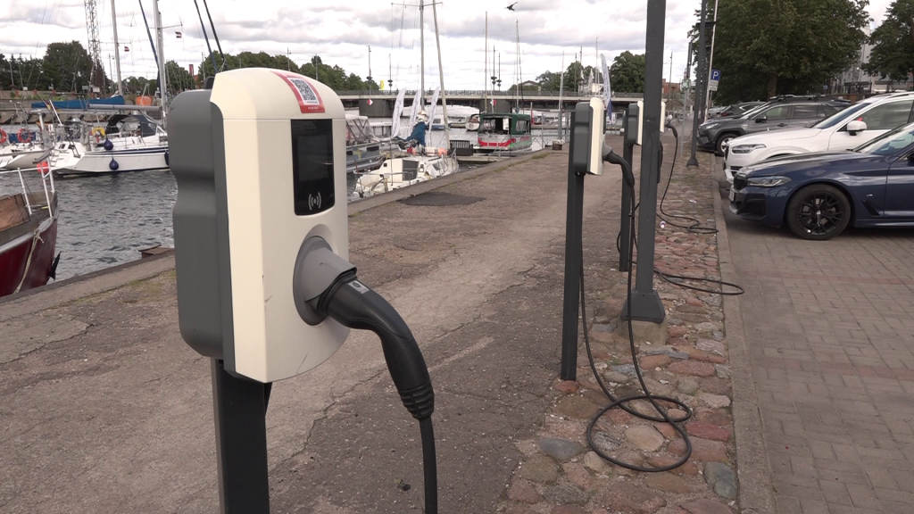 Elektroauto uzlādes stacija ar kabeļiem pie upes vai ostas