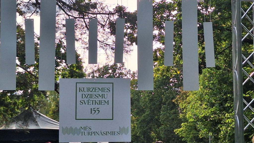 Plakāts ar uzrakstu "Kurzemes Dziesmu svētkiem 155".