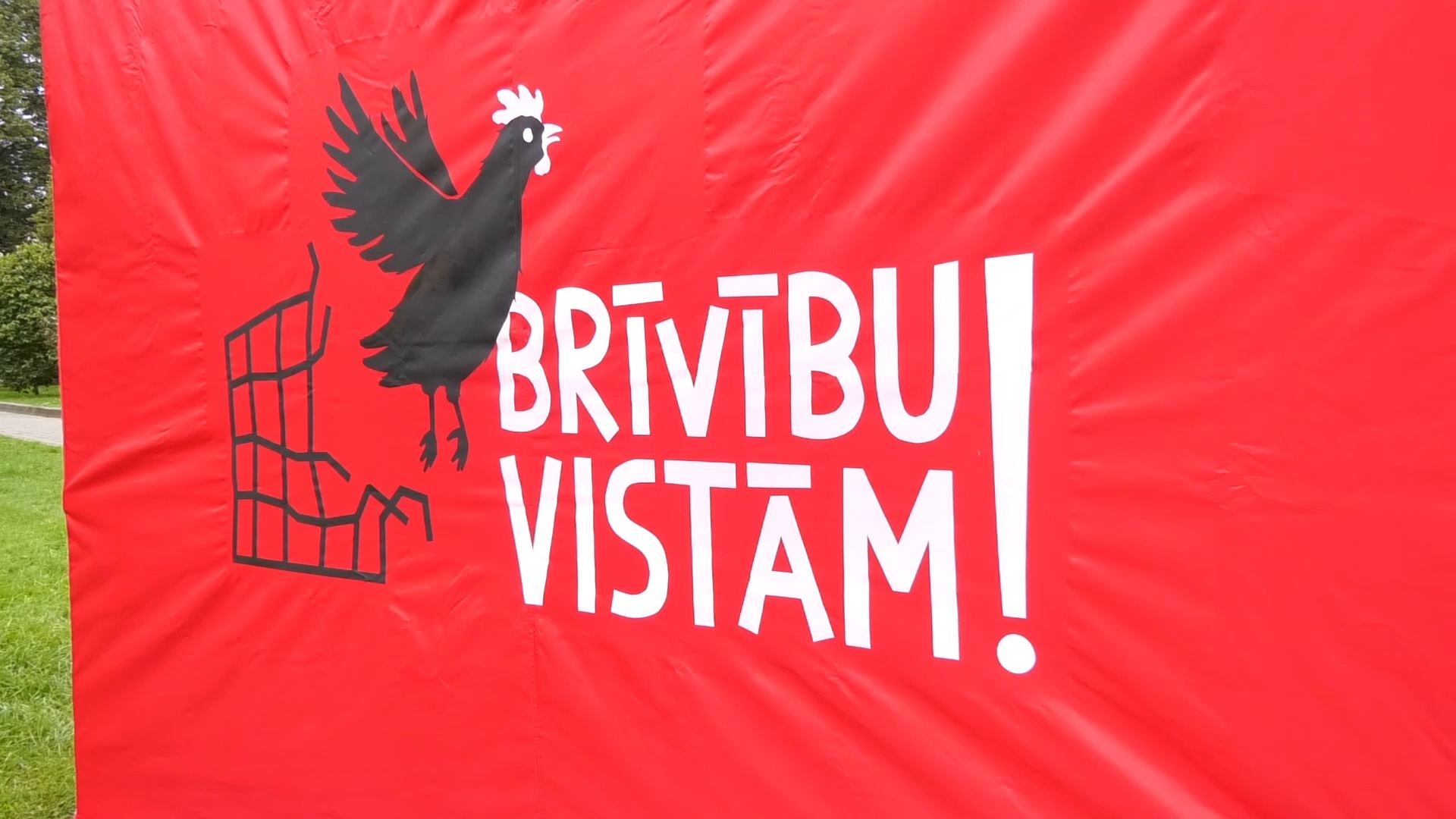 Sarkans plakāts ar uzrakstu “Brīvību vistām!” un vistas attēlu.