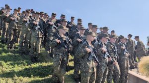 Latvijas karavīri formā stāv ierindā ar ieročiem rokās