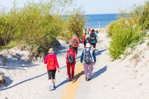 Cilvēku grupa dodas TrekTours pārgājienā pa piejūras taku uz pludmali.