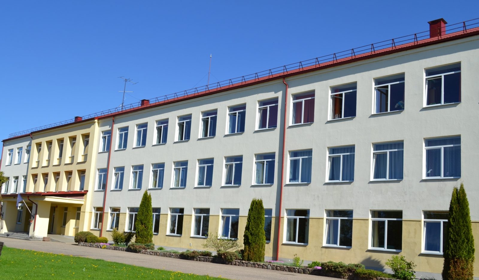 Aglonas vidusskolas ēka saulainā dienā ar sakoptu apkārtni.