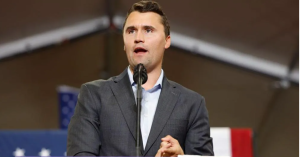 Čārlijs Kērks runā publiskā pasākumā pie mikrofona.