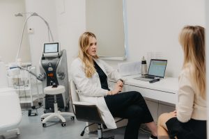 Estētiskās medicīnas ārste sarunājas ar pacienti klīnikas kabinetā