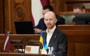 Andris Šuvajevs uzstājas Saeimas sēdē pie tribīnes ar Latvijas un Ukrainas karogu priekšplānā.