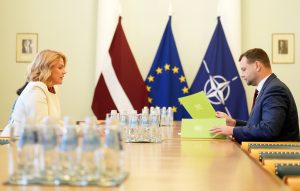 Ministru prezidente Evika Siliņa tiekas ar labklājības ministru Reini Uzulnieku pie konferenču galda ar Latvijas, Eiropas Savienības un NATO karogiem fonā.