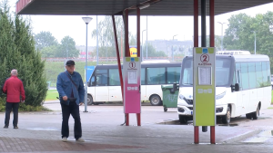 Cilvēki pie autobusu pieturvietām ar platformu numuriem un stāvošiem autobusiem