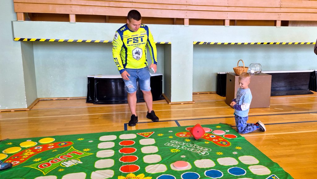 Vīrietis un zēns spēlē lielo Ludo spēli uz grīdas.